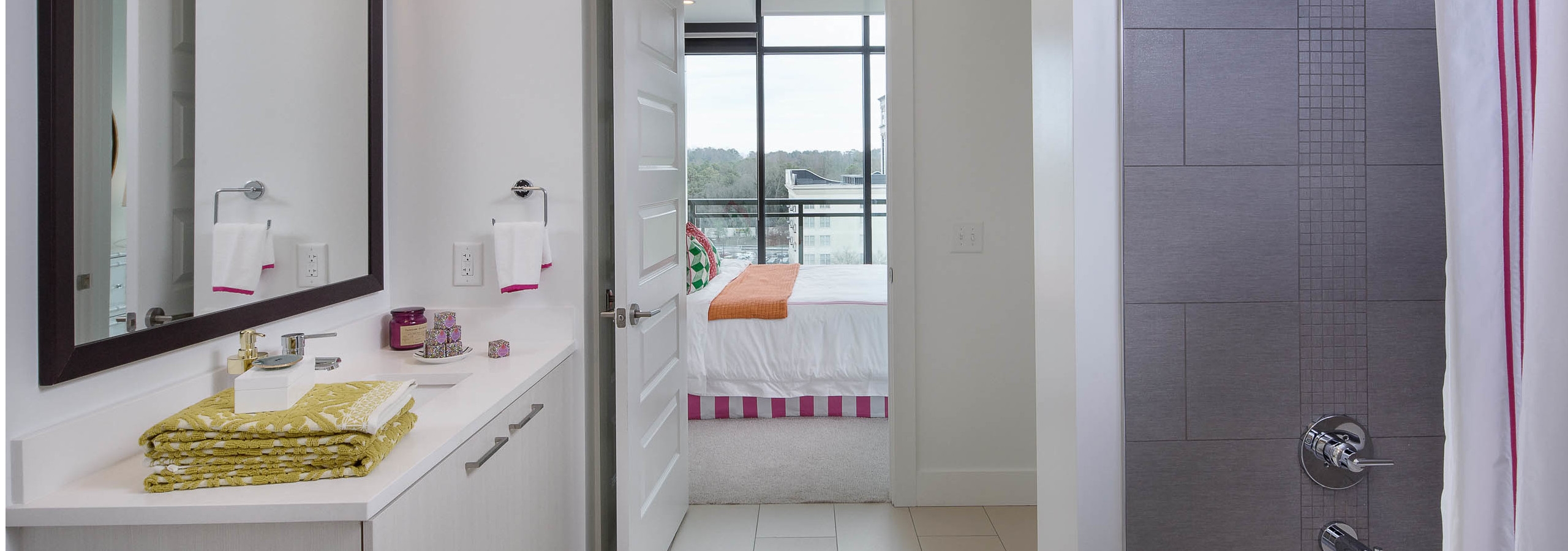 Bathroom at AMLI 3464 with white vanity sink and a grey tiled shower with an open door peaking into the connected bedroom