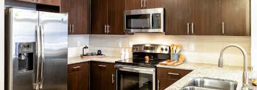 AMLI West Plano kitchen with dark cabinets and granite countertops with stainless steel appliances and sleek white backsplash