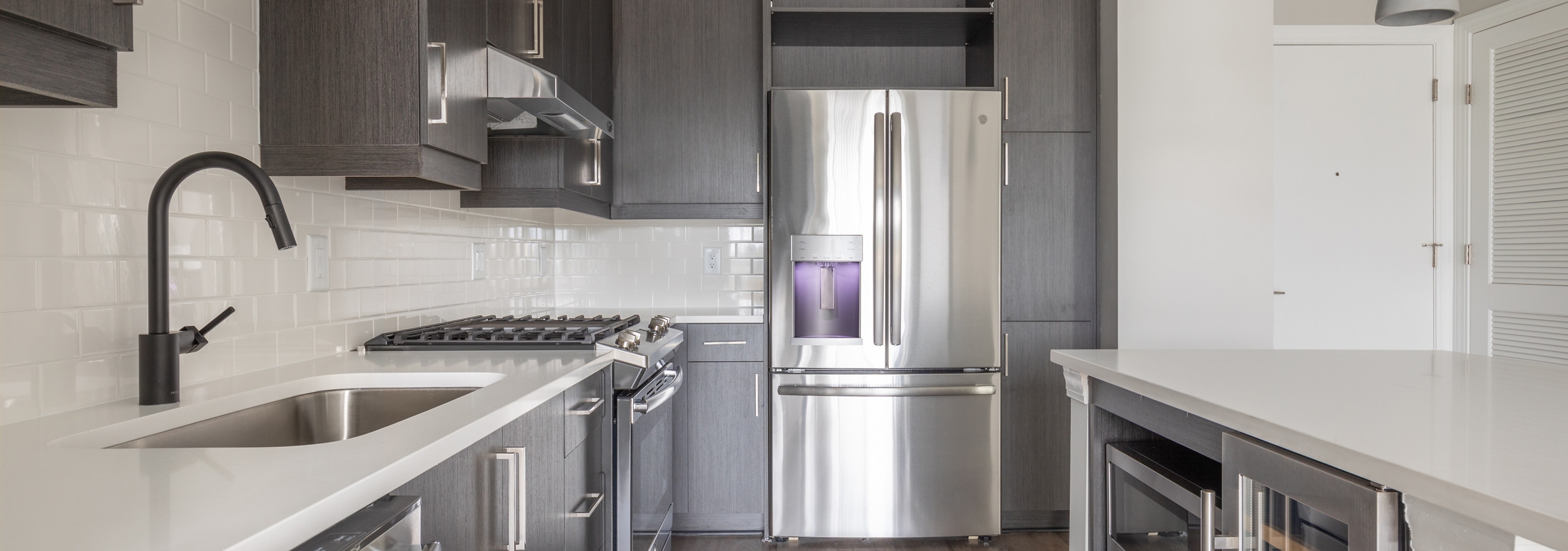 AMLI Westside kitchen with dark grey cabinets and white countertops with gas stovetop and premium  stainless steel appliances