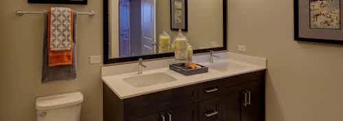 Interior view of AMLI Deerfield bathroom with double vanity sinks and white countertops with dark espresso wood cabinets