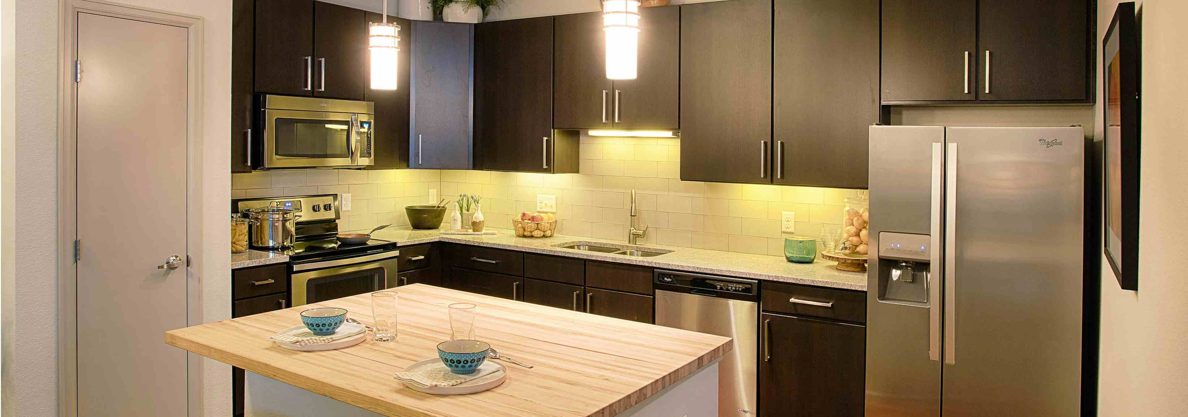 A kitchen at AMLI Denargo Market apartments with an island and a stainless steel fridge and several cabinets and a closet