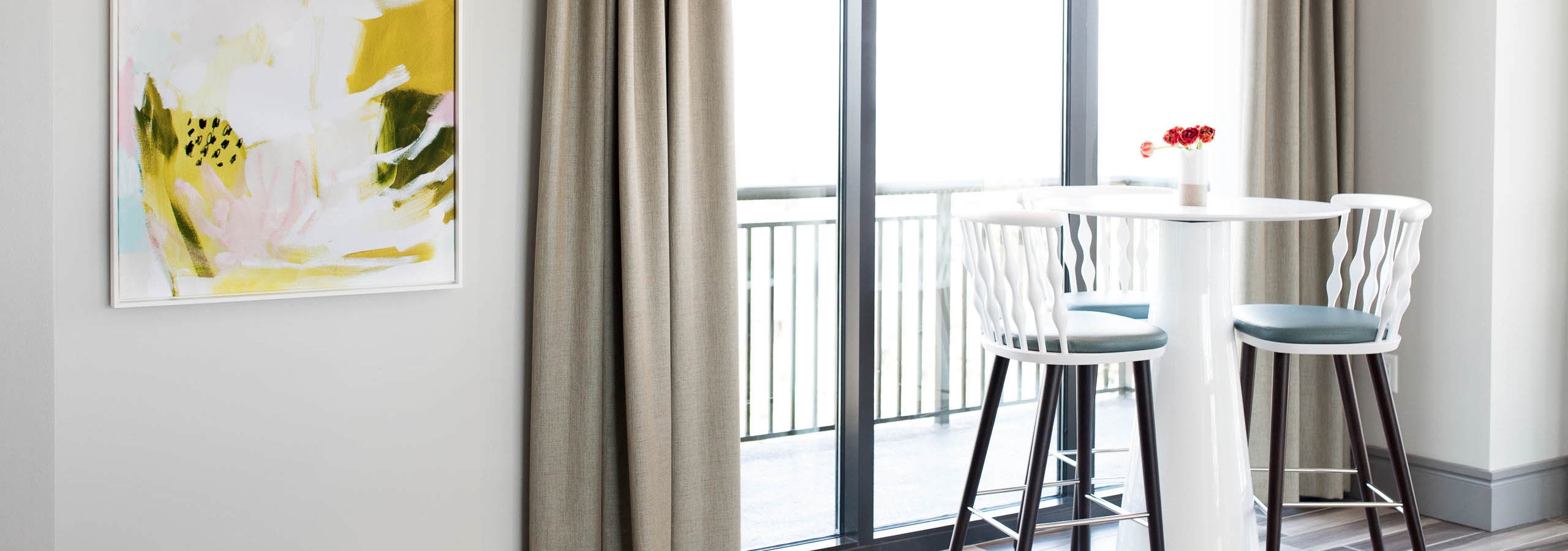Raised white table with barstools by a tall window in the AMLI 3464 clubroom with a yellow art piece hanging on the wall