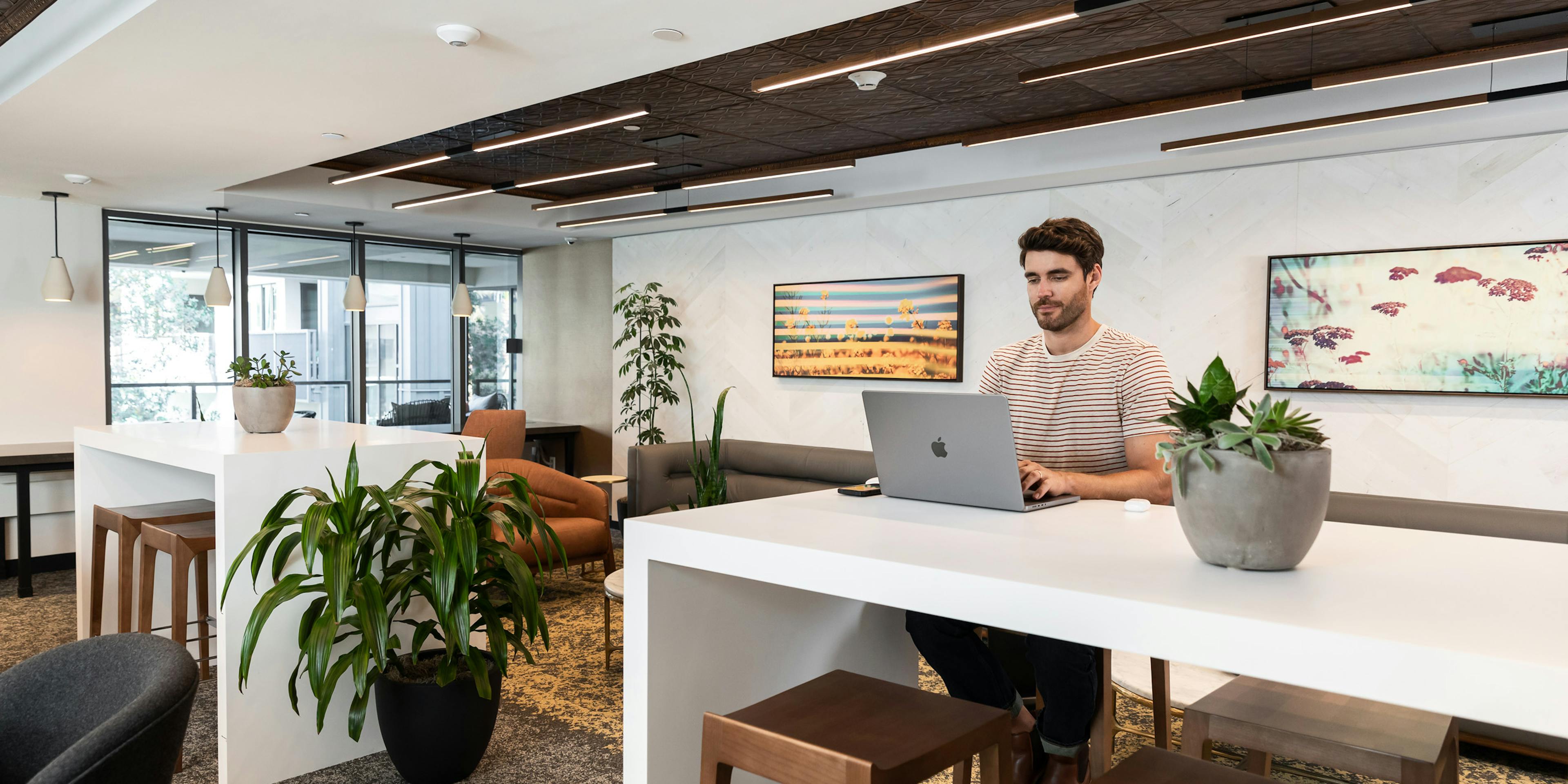 Interior view of the business center at AMLI Old Pasadena and a man sitting peacefully at a white work desk with his laptop