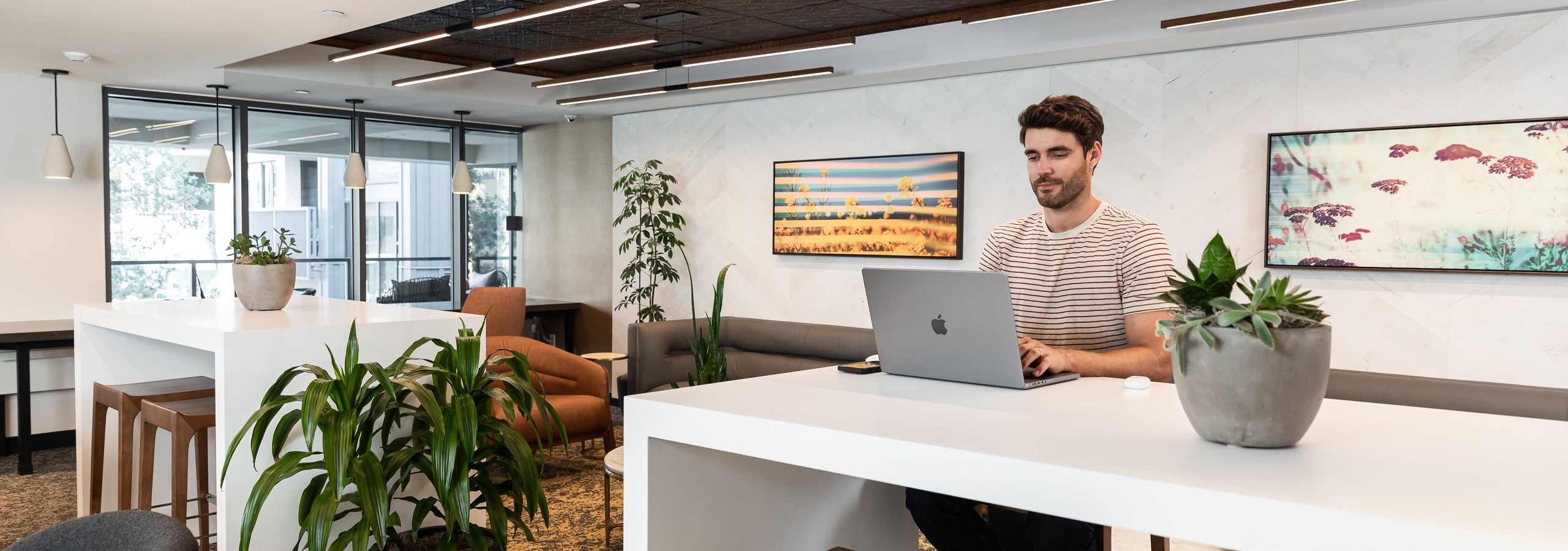 Interior view of the business center at AMLI Old Pasadena and a man sitting peacefully at a white work desk with his laptop