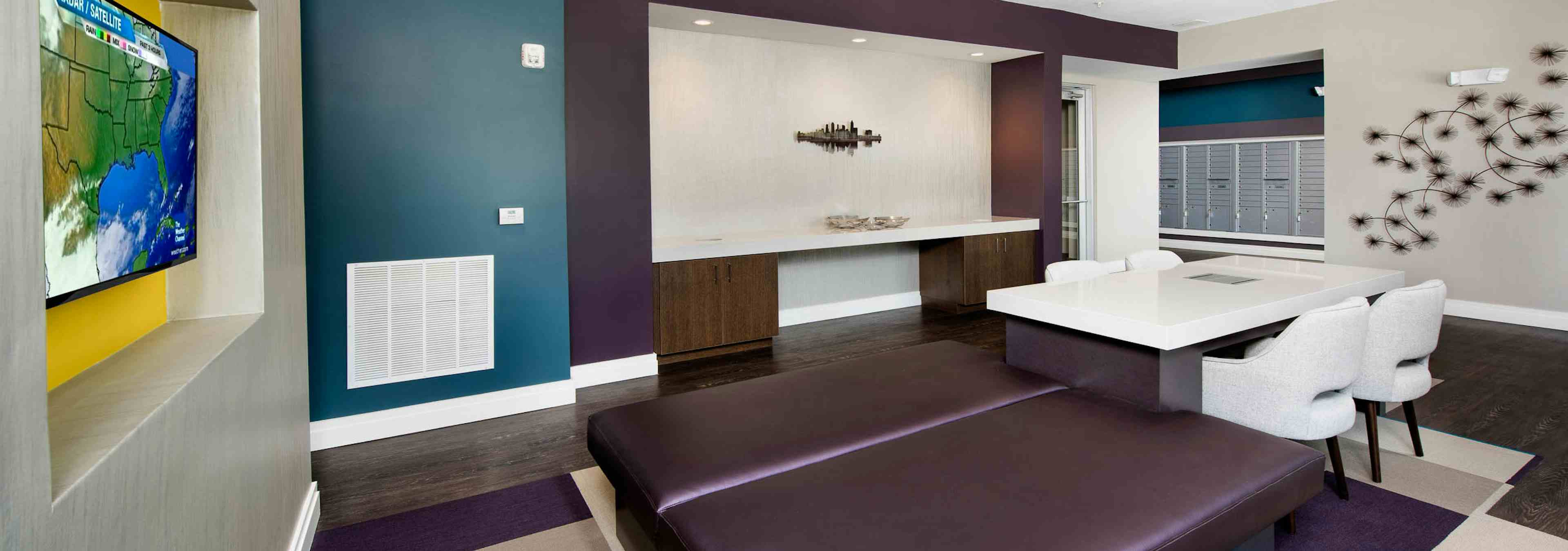 AMLI Buckhead mailroom with dark wood floors and a white table and chairs with teal and plum accent walls and a large TV