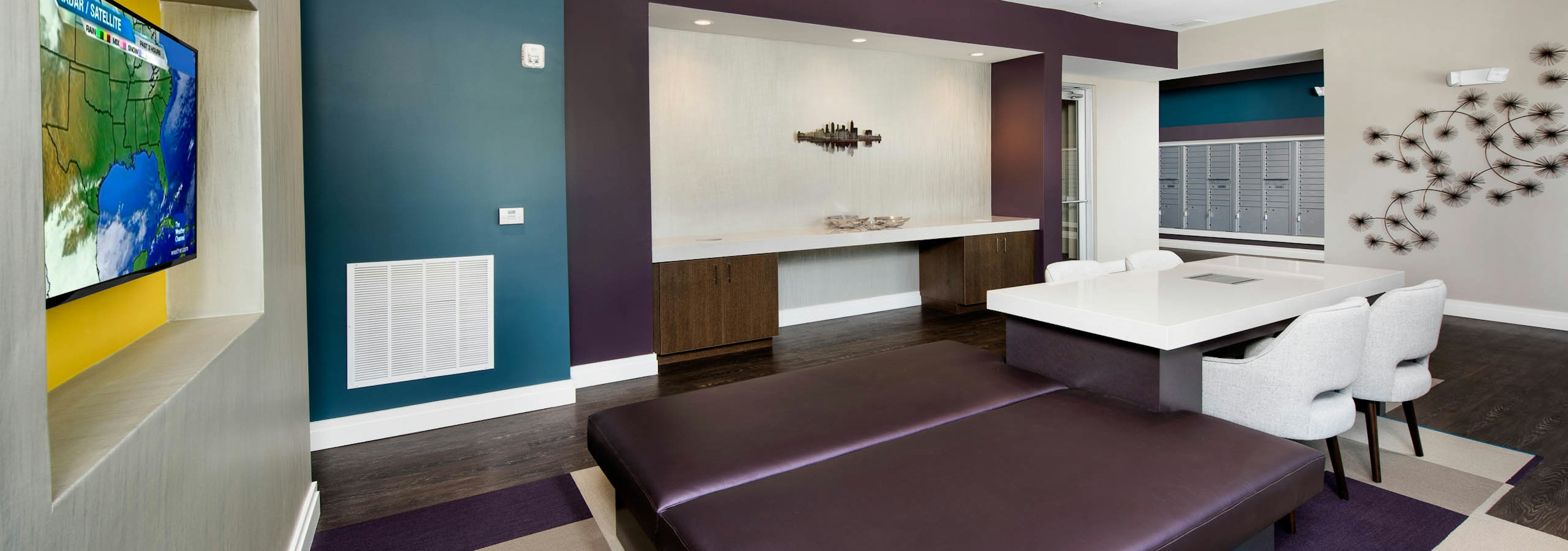 AMLI Buckhead mailroom with dark wood floors and a white table and chairs with teal and plum accent walls and a large TV