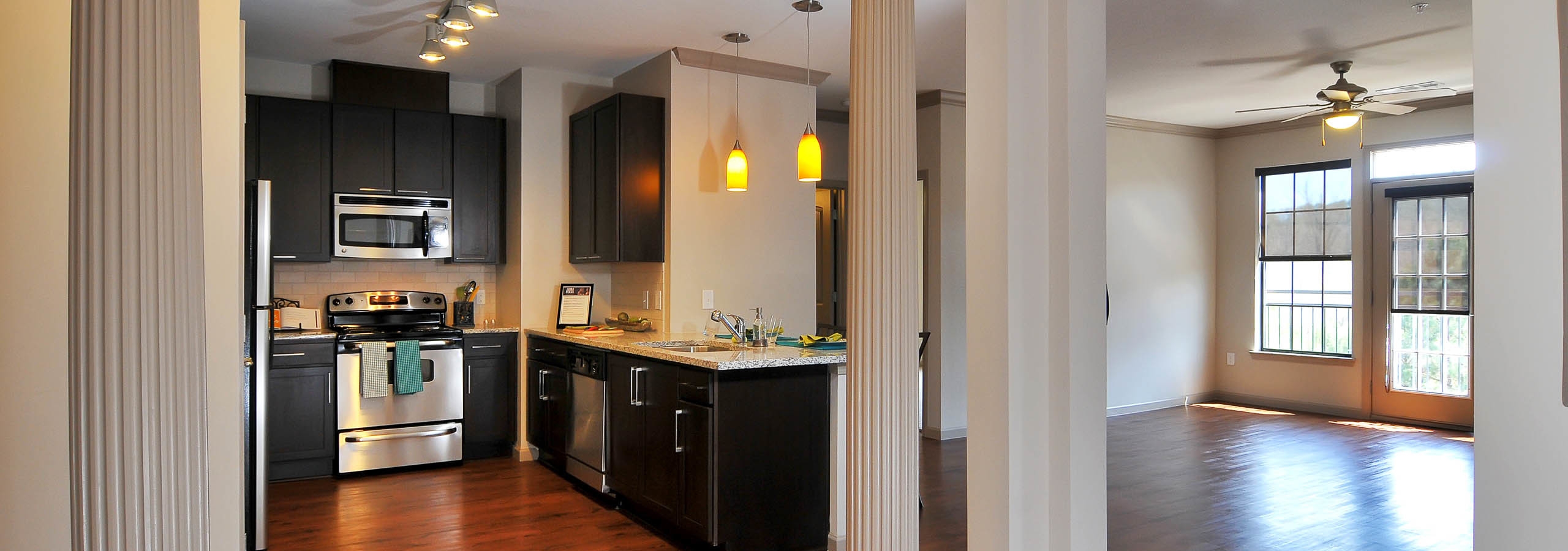 AMLI North Point kitchen with dark cabinets and modern light fixtures with empty living area and windows in the background