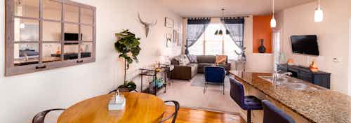 A kitchen and living room at AMLI Arista apartments with dinner table and large mirror and counter top with chairs and couch