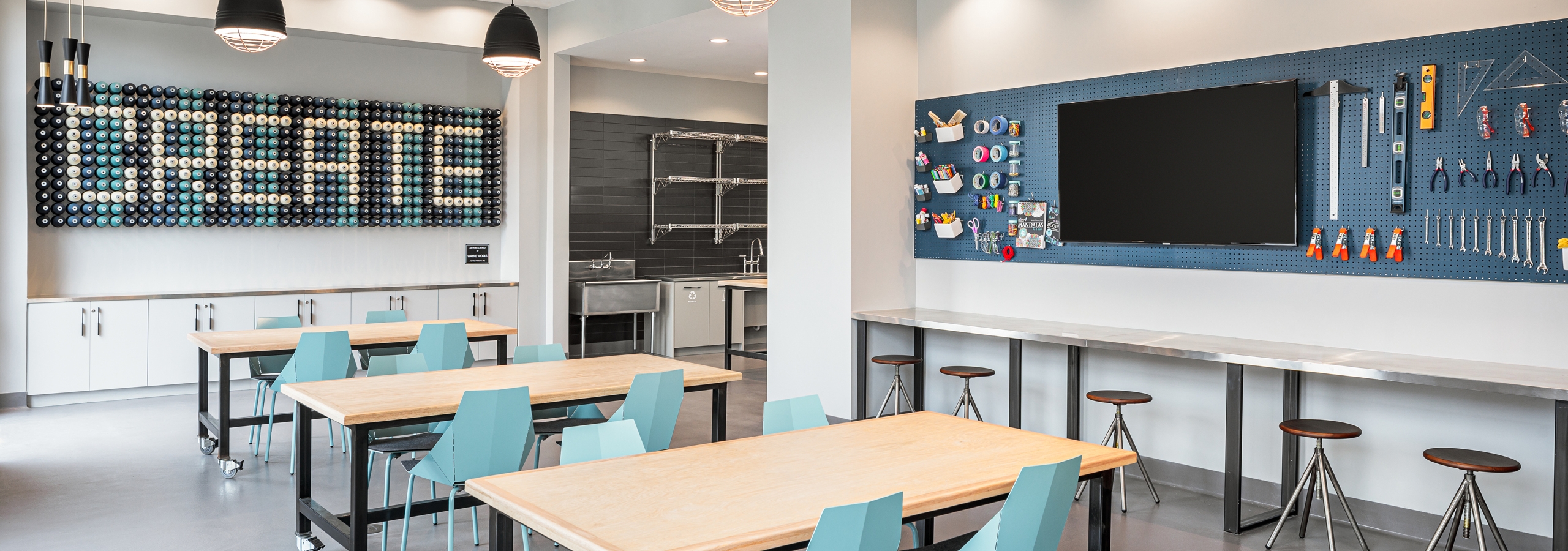 Maker space at AMLI Addison with tables and barstool seating with a variety of tools to create with hanging on the wall