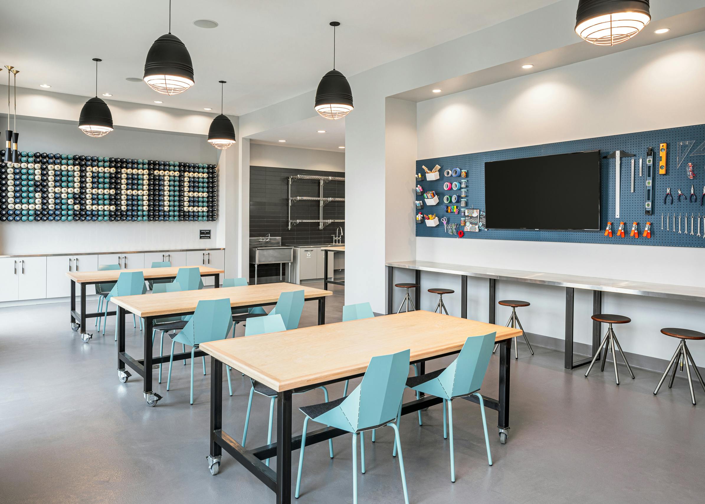 Maker space at AMLI Addison with tables and barstool seating with a variety of tools to create with hanging on the wall