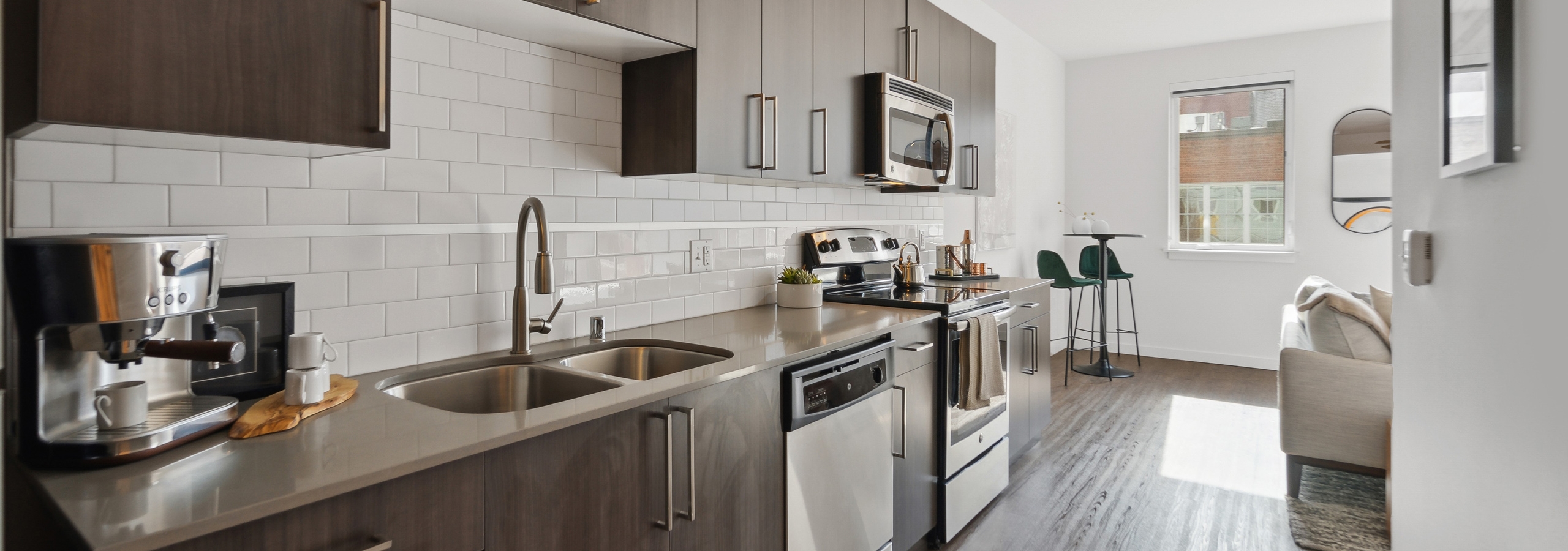 Kitchen at AMLI South Lake Union with white tile backsplash and brown wood grain cabinets and a peek into the living room