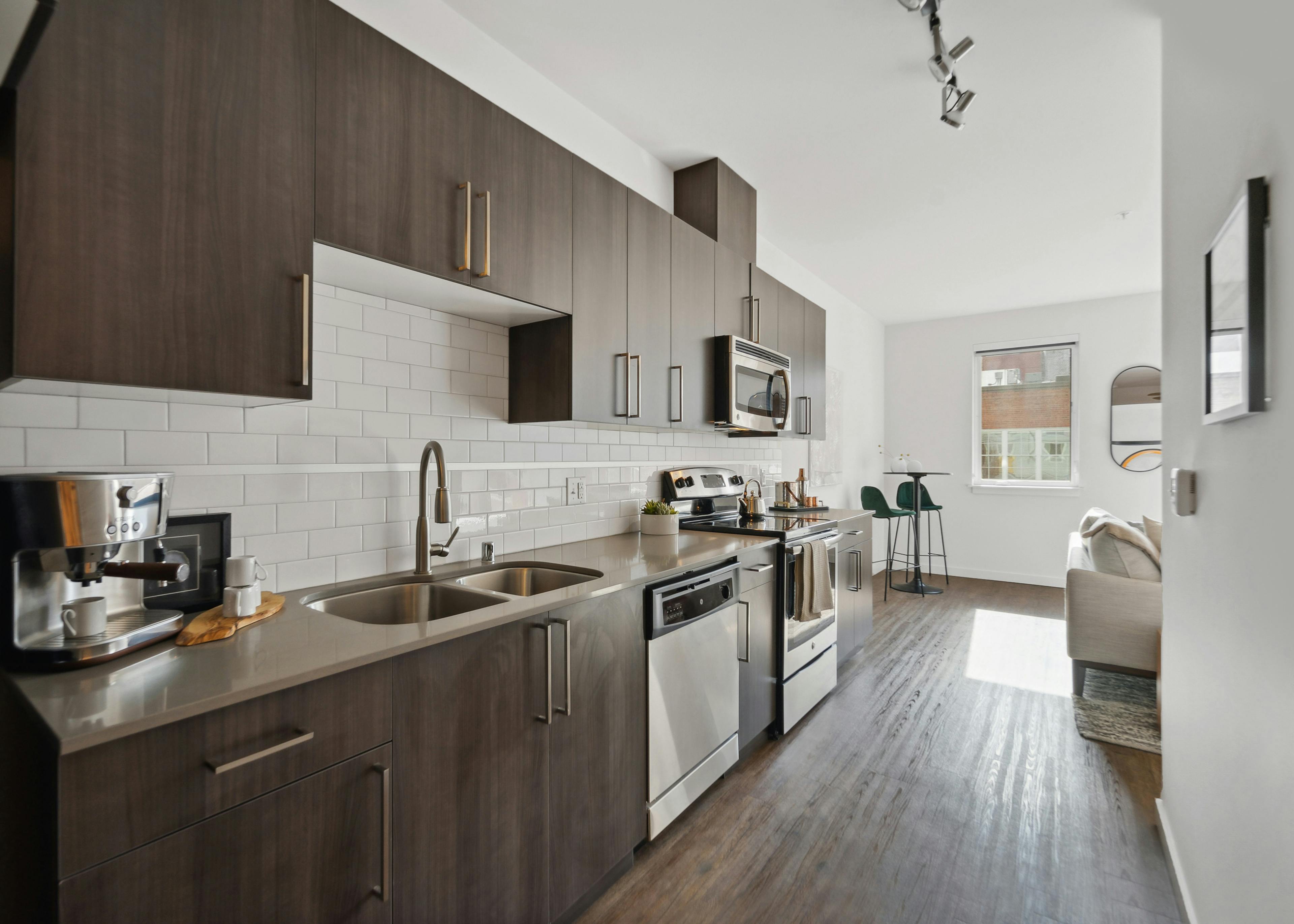 Kitchen at AMLI South Lake Union with white tile backsplash and brown wood grain cabinets and a peek into the living room