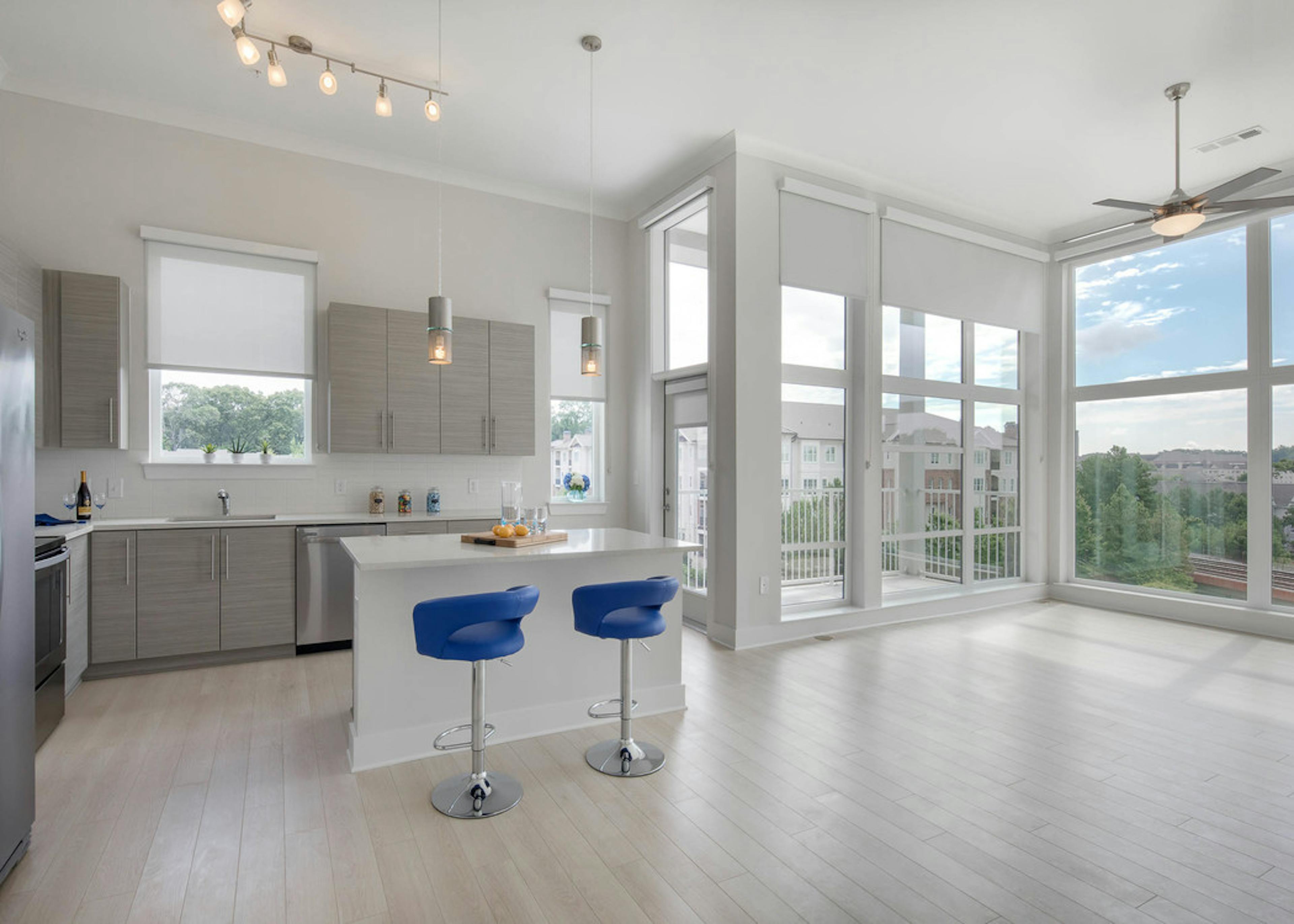 AMLI Buckhead kitchen with grey wood cabinets and an island with blue barstools and floor to ceiling windows with nature view