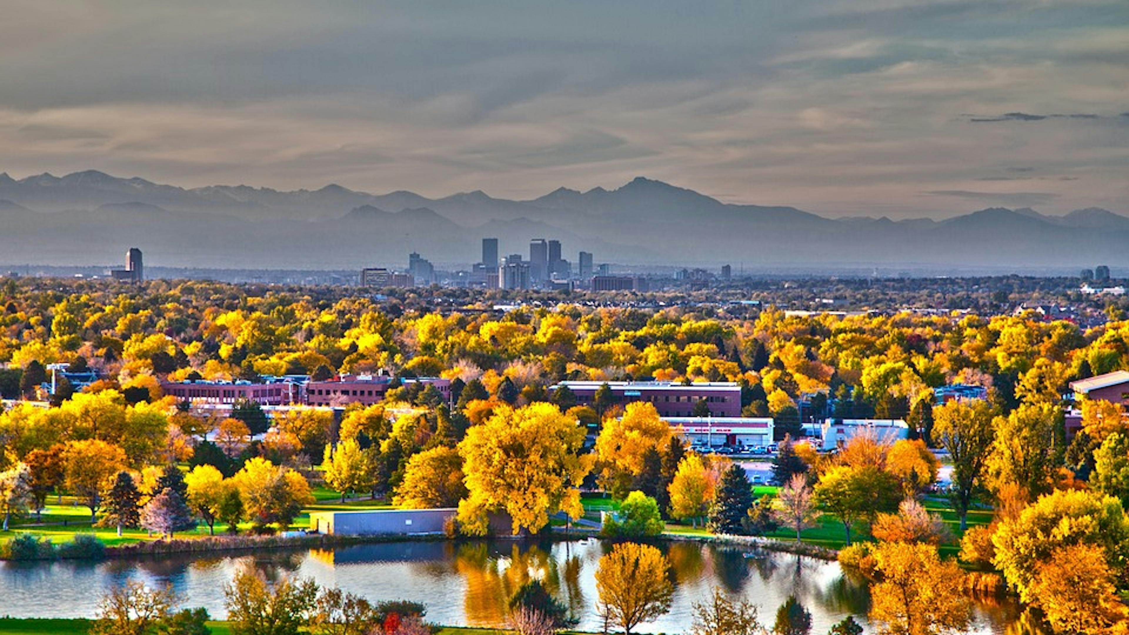 A panoramic image of a lake in front of downtown Denver with the mountains in the background