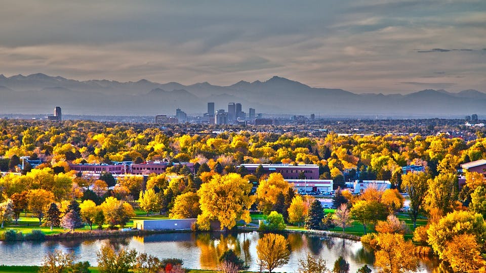 A panoramic image of a lake in front of downtown Denver with the mountains in the background