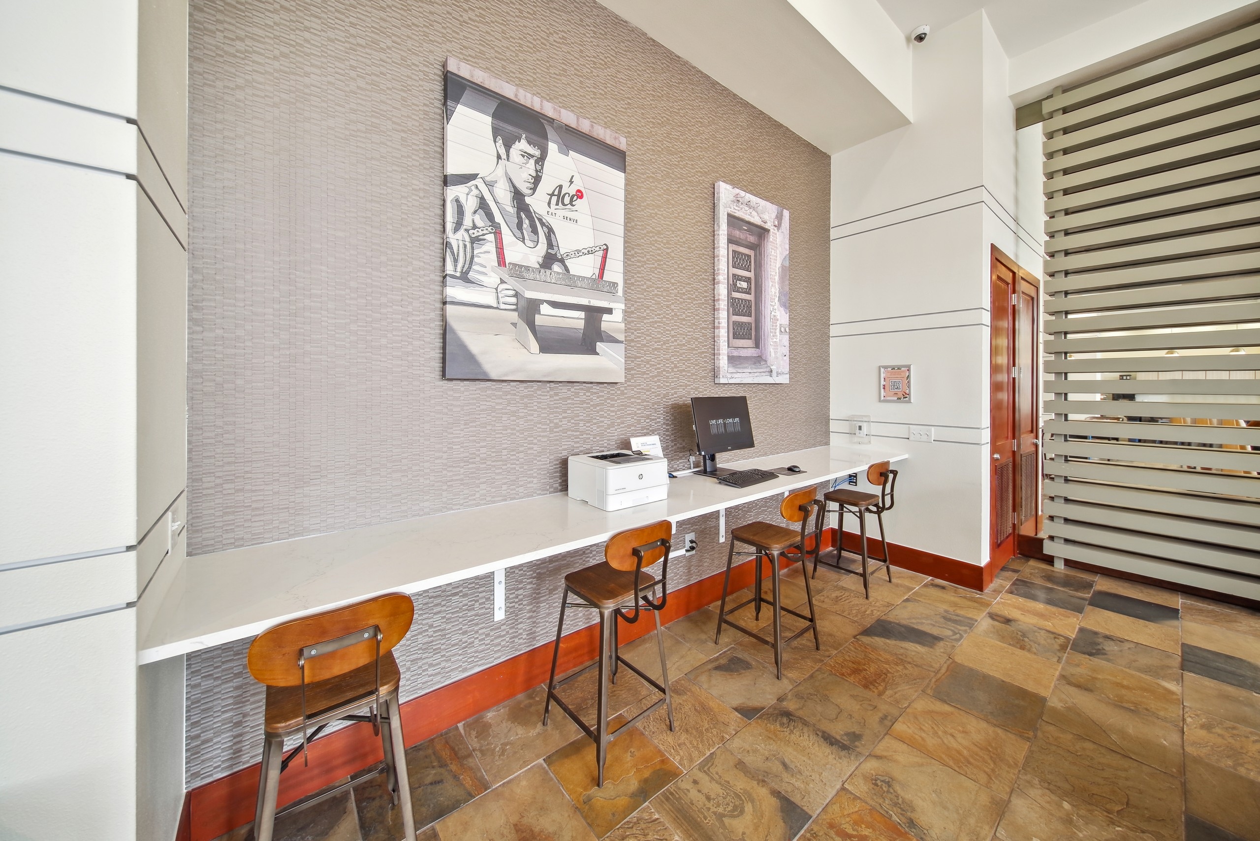 A business center at AMLI Park Avenue featuring a computer and printer with high top wooden chairs and two canvas art pieces