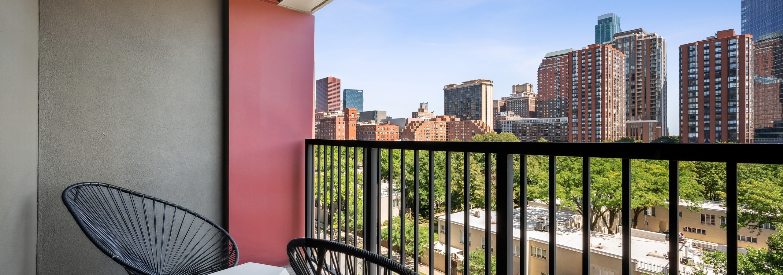 AMLI 900 apartment balcony with two round wire chairs and modern table and brown railing with view of city buildings