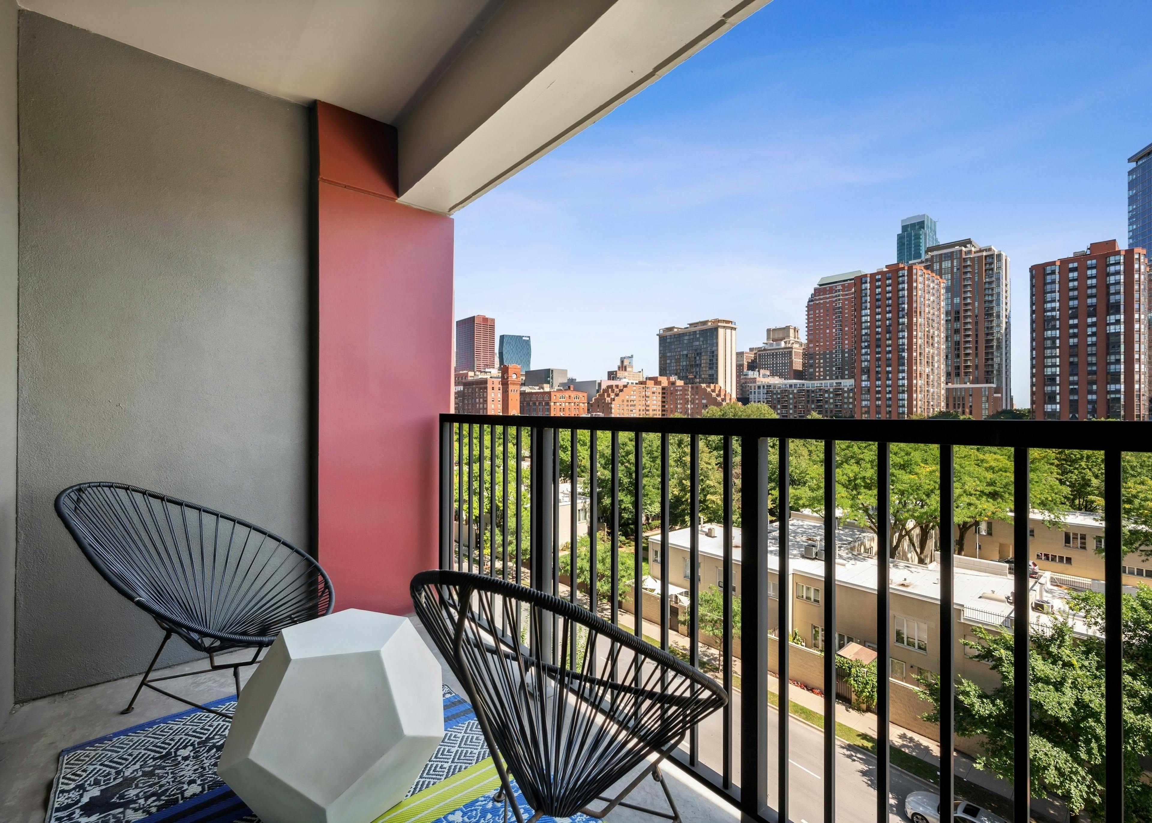 AMLI 900 apartment balcony with two round wire chairs and modern table and brown railing with view of city buildings