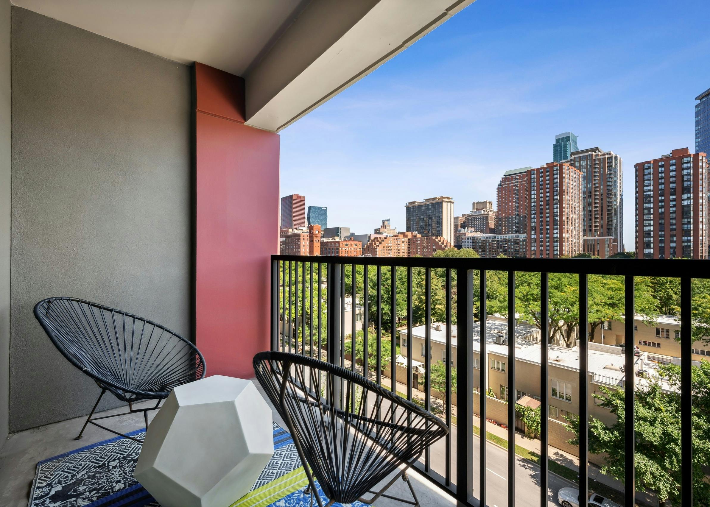 AMLI 900 apartment balcony with two round wire chairs and modern table and brown railing with view of city buildings