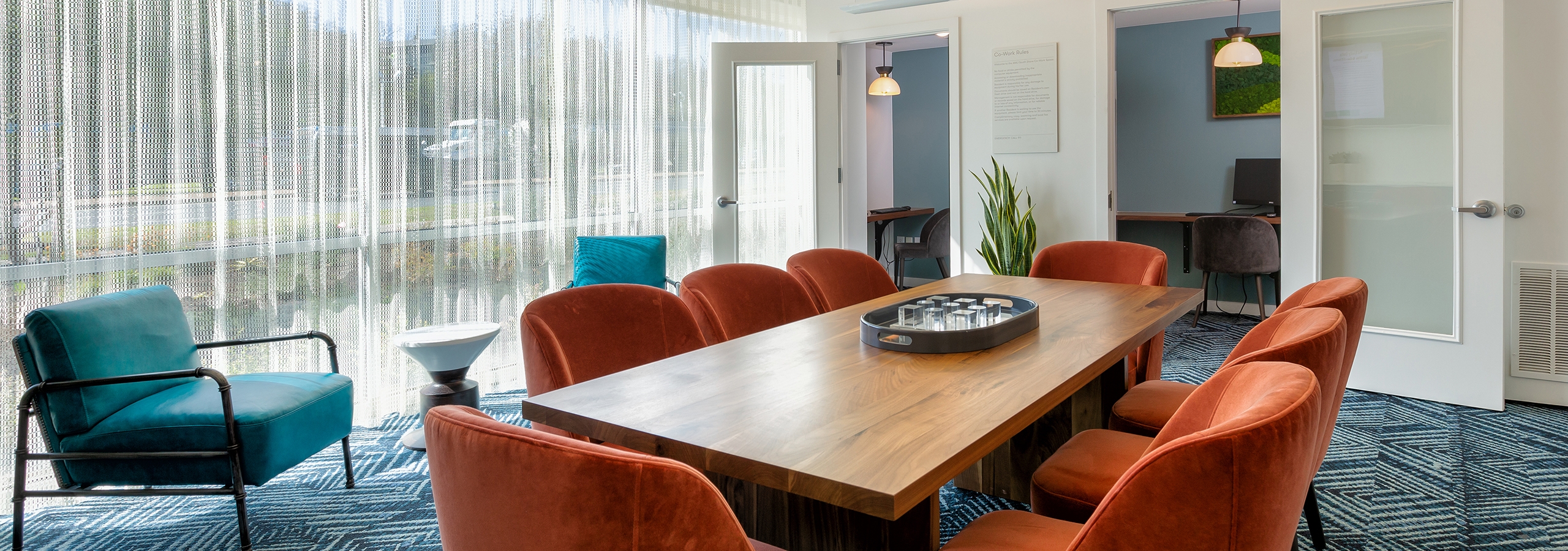 AMLI South Shore co working space with orange office chairs around wooden table with blue carpet and floor to ceiling windows
