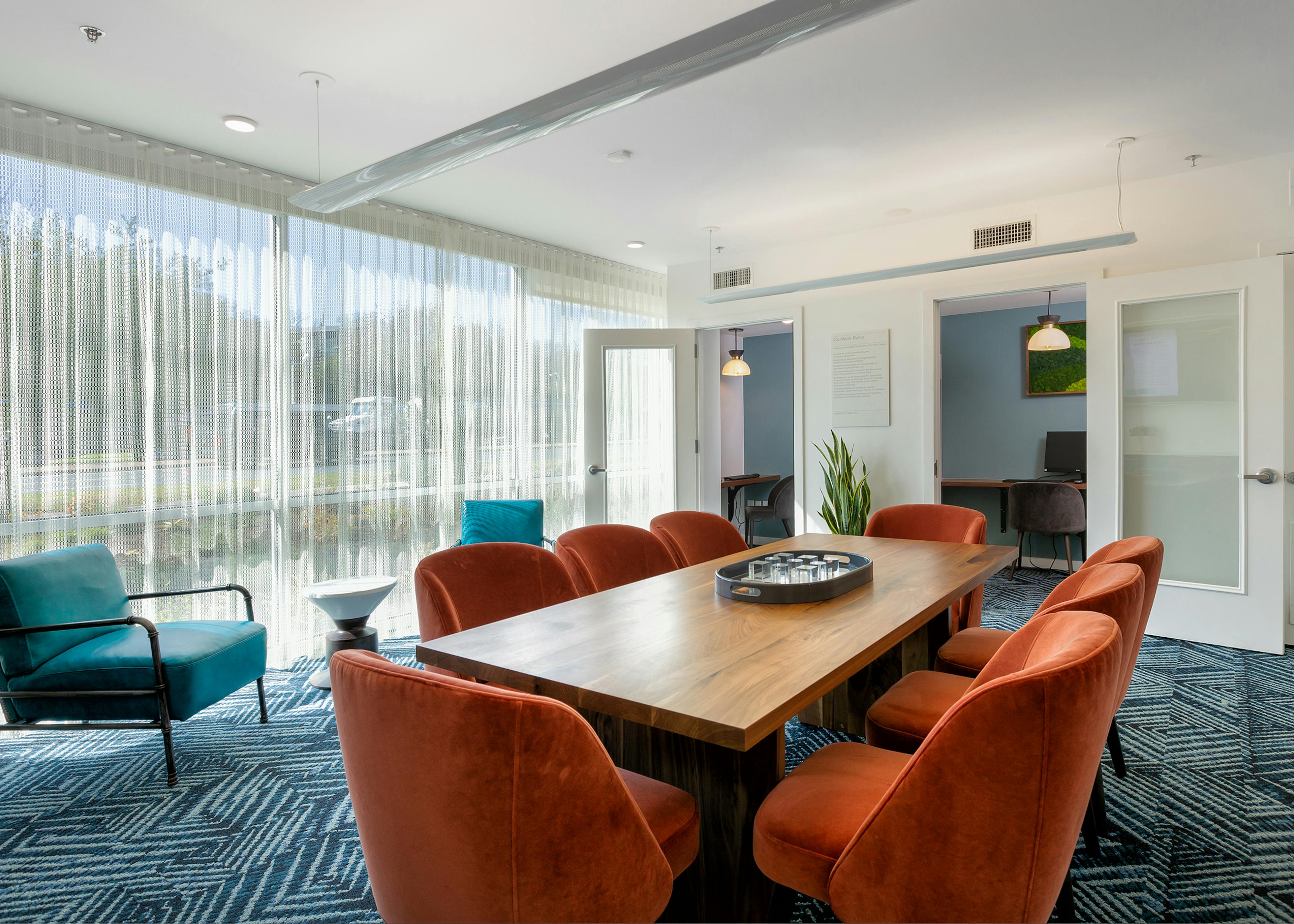 AMLI South Shore co working space with orange office chairs around wooden table with blue carpet and floor to ceiling windows