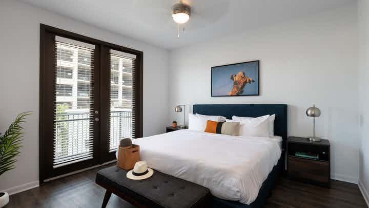 Interior of AMLI 300 apartment bedroom with private balcony and large windows with shades and a ceiling fan