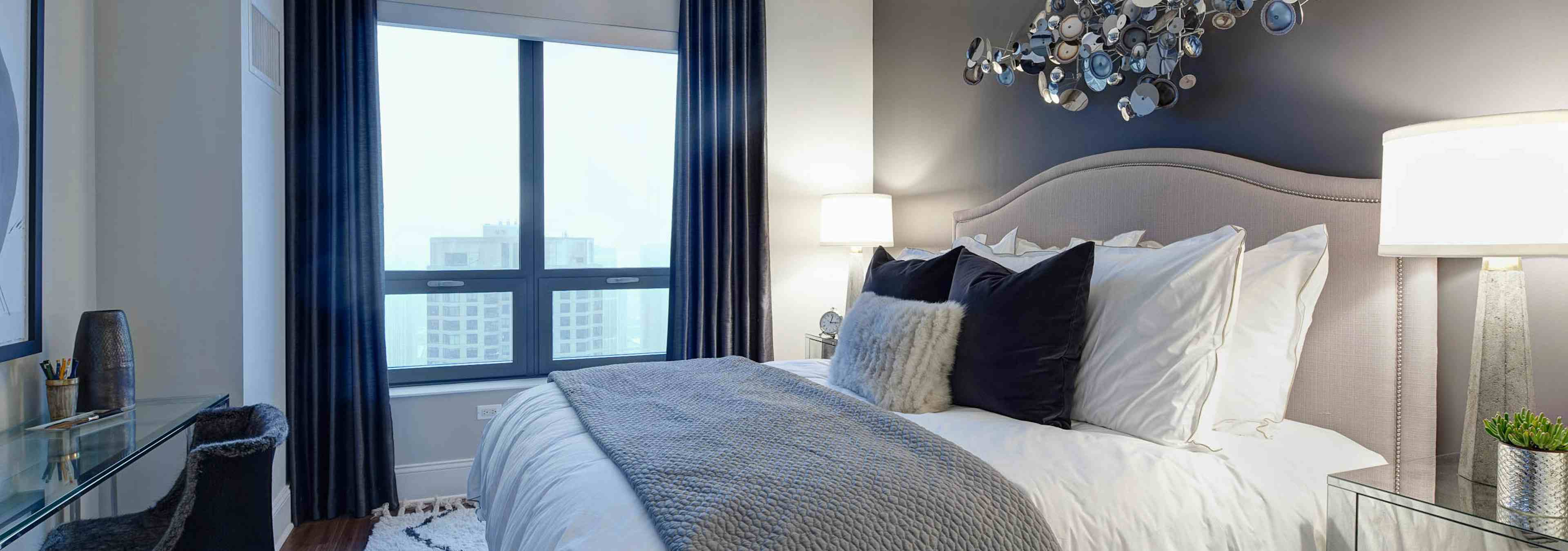 Penthouse bedroom at AMLI River North with a dark accent wall that a beige heardboard is leaning against with white bedding