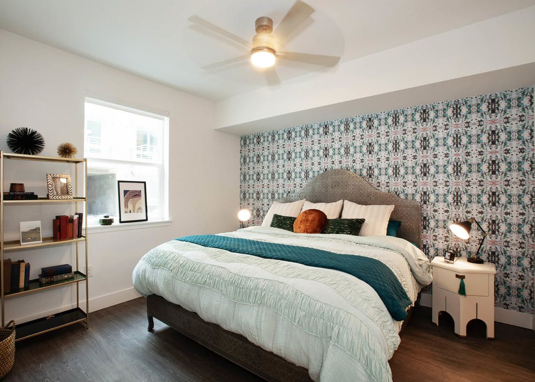 Interior of AMLI Park Broadway apartment bedroom with patterned wall paper behind a king size bed and night stand with lamp