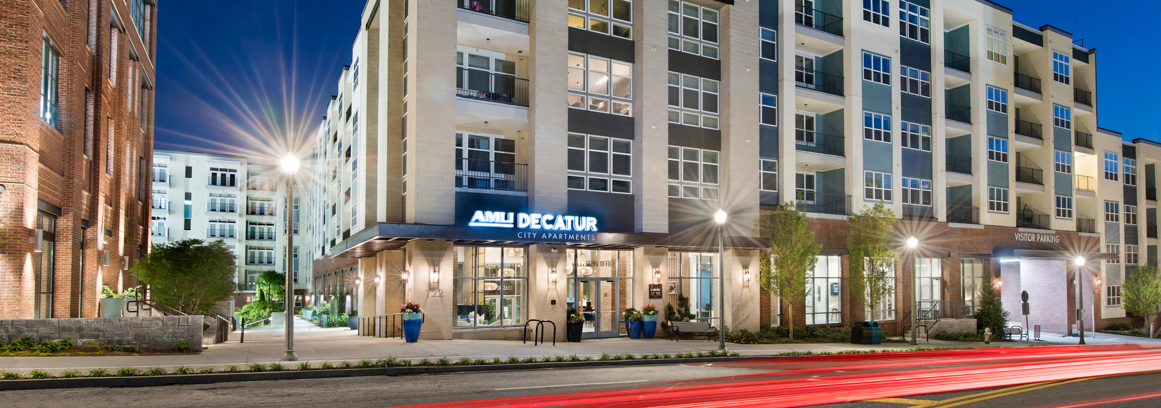 Nighttime view of AMLI Decatur apartment building with stucco and brick facade and lamp posts and trees lining the building