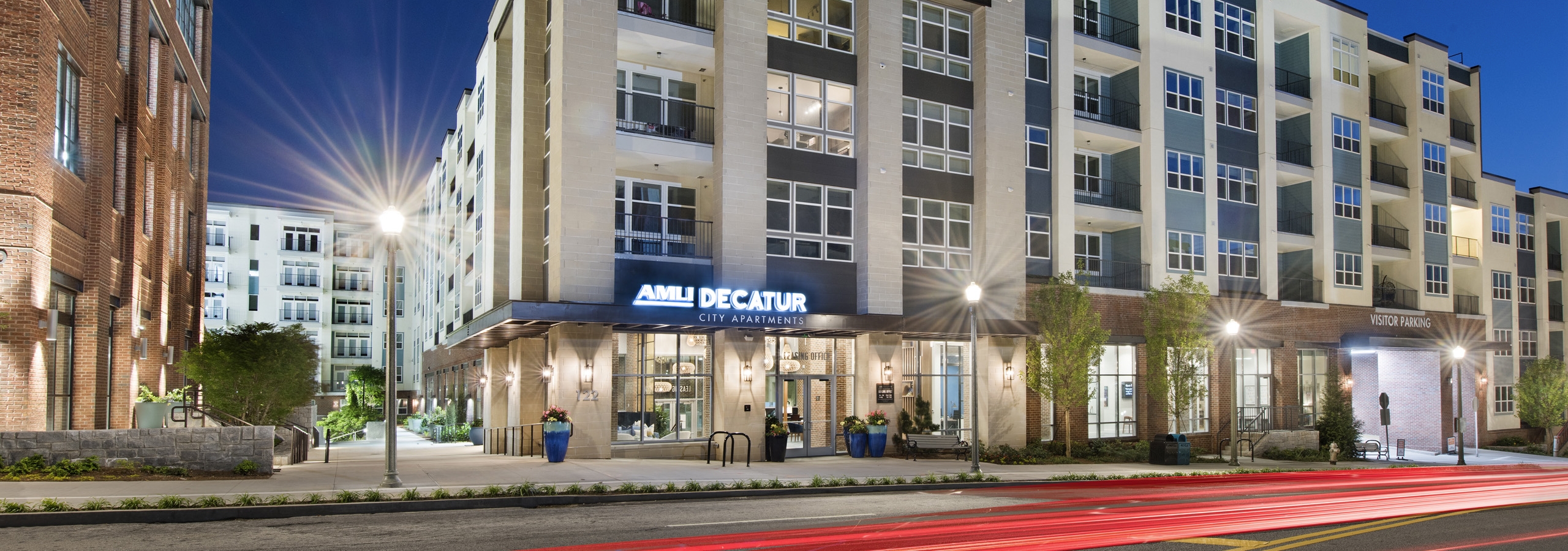 Nighttime view of AMLI Decatur apartment building with stucco and brick facade and lamp posts and trees lining the building