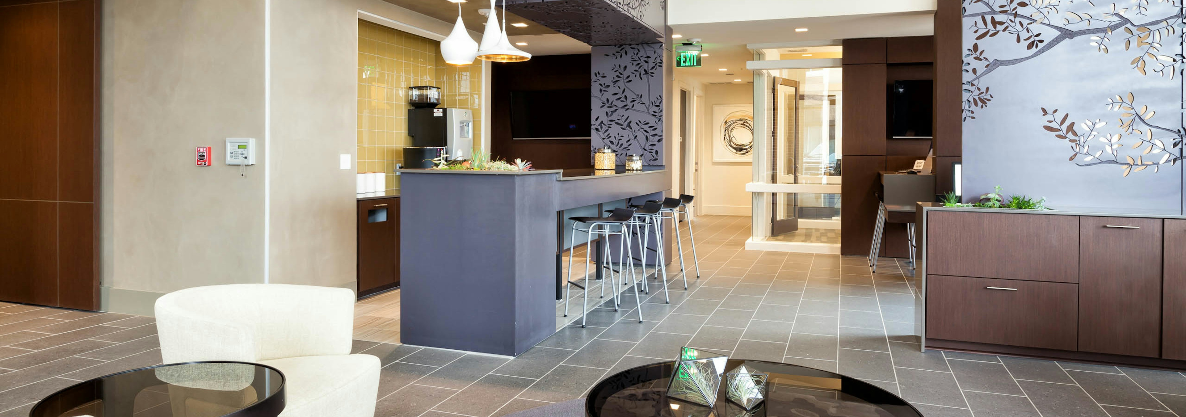 AMLI West Plano clubroom with close up of coffee tables and white chair with beige tile flooring and view of a java cafe area