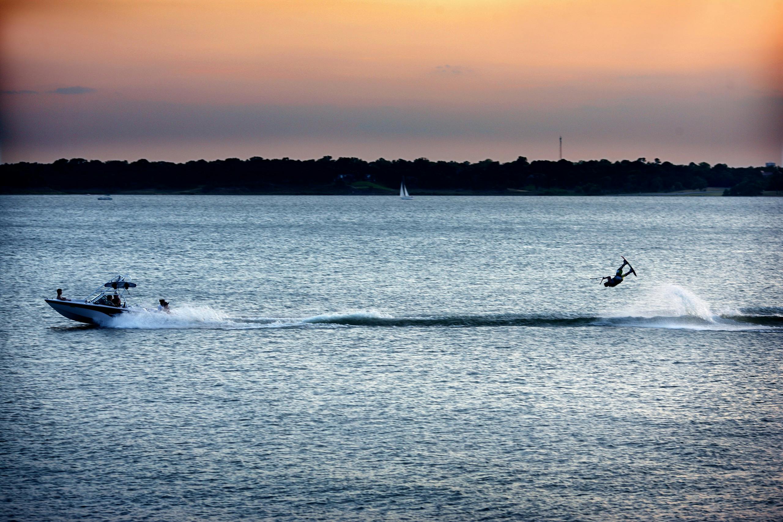 A lake at sunset with a boat racing across the water pulling a man on a wakeboard