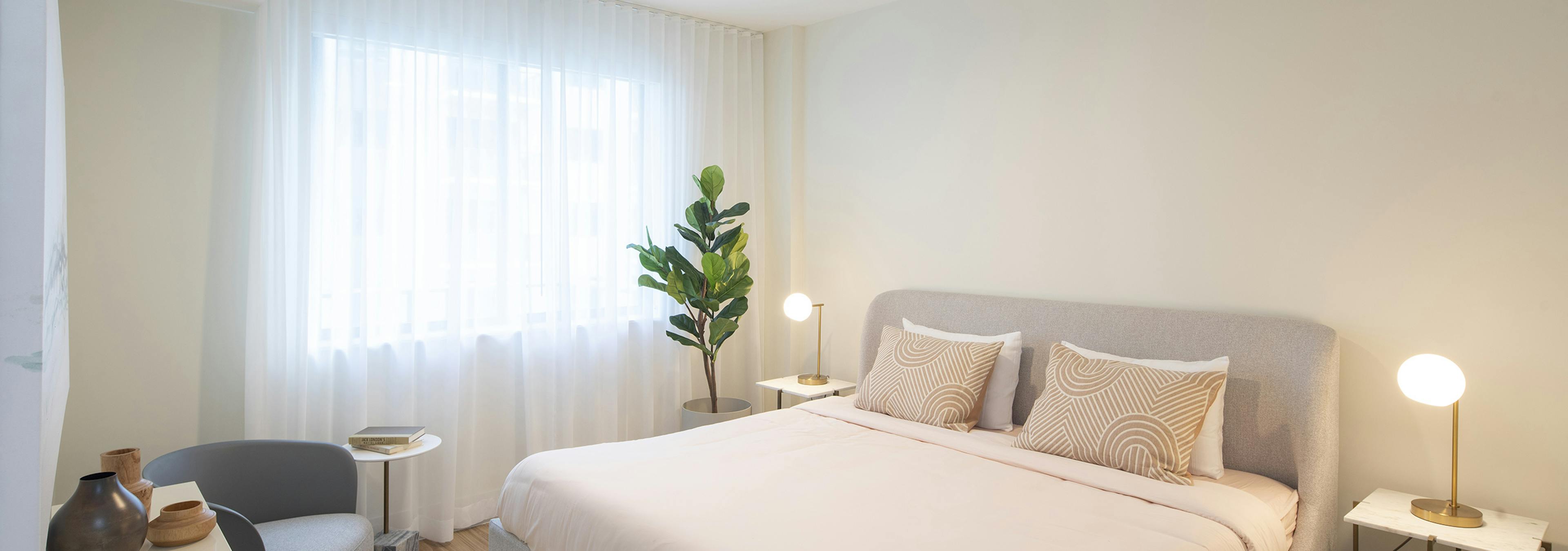 AMLI Midtown Miami apartment bedroom with bed and two nightstands with lamps and plant in front of curtained window