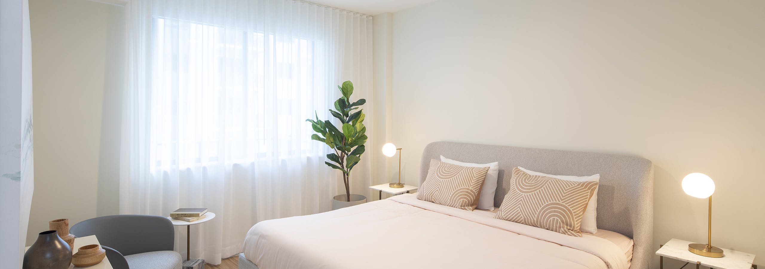 AMLI Midtown Miami apartment bedroom with bed and two nightstands with lamps and plant in front of curtained window