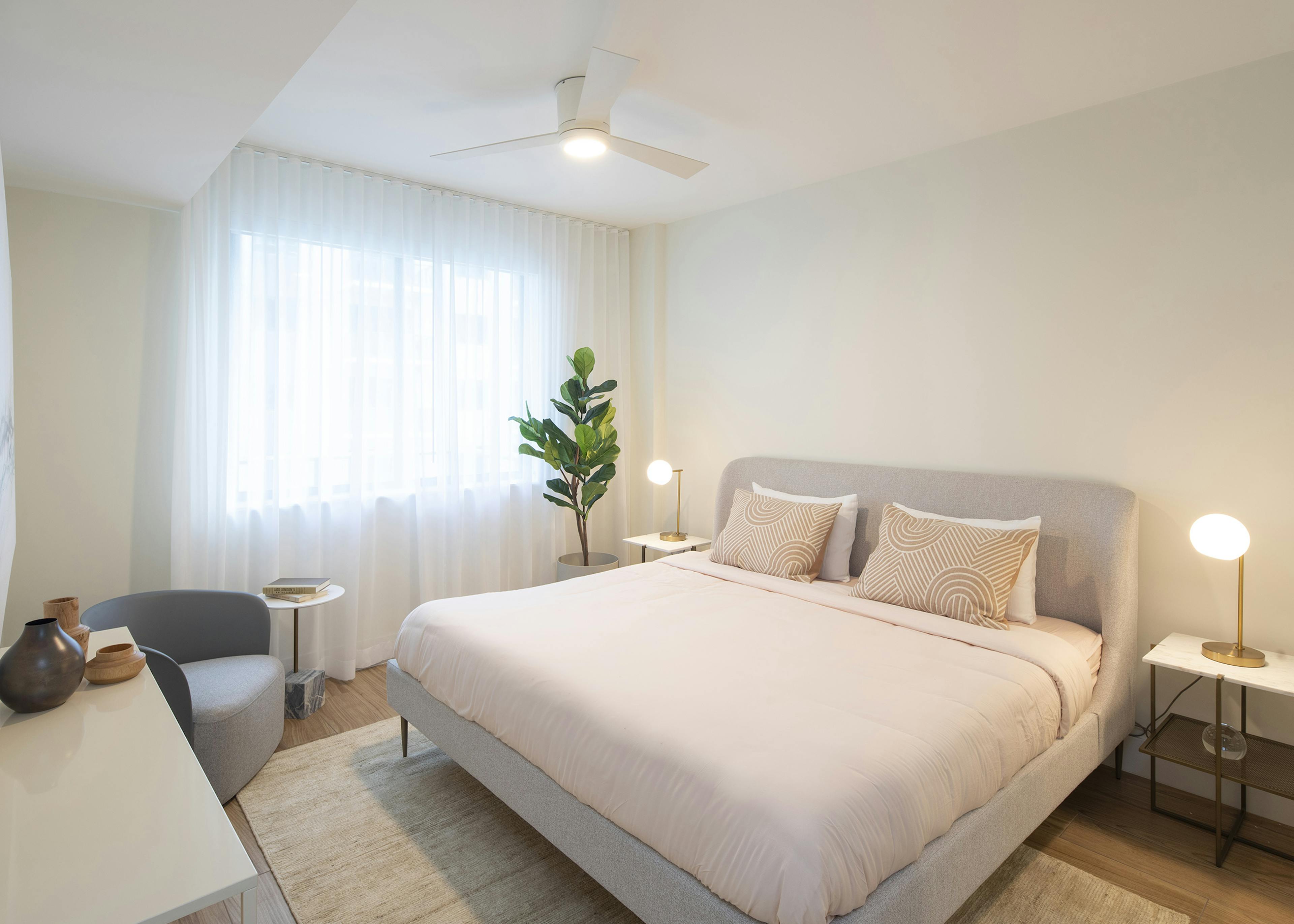 AMLI Midtown Miami apartment bedroom with bed and two nightstands with lamps and plant in front of curtained window
