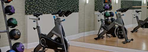 Close up view of fitness center at AMLI Evanston with exercise bike and shelved weights in front of a large wall mirror