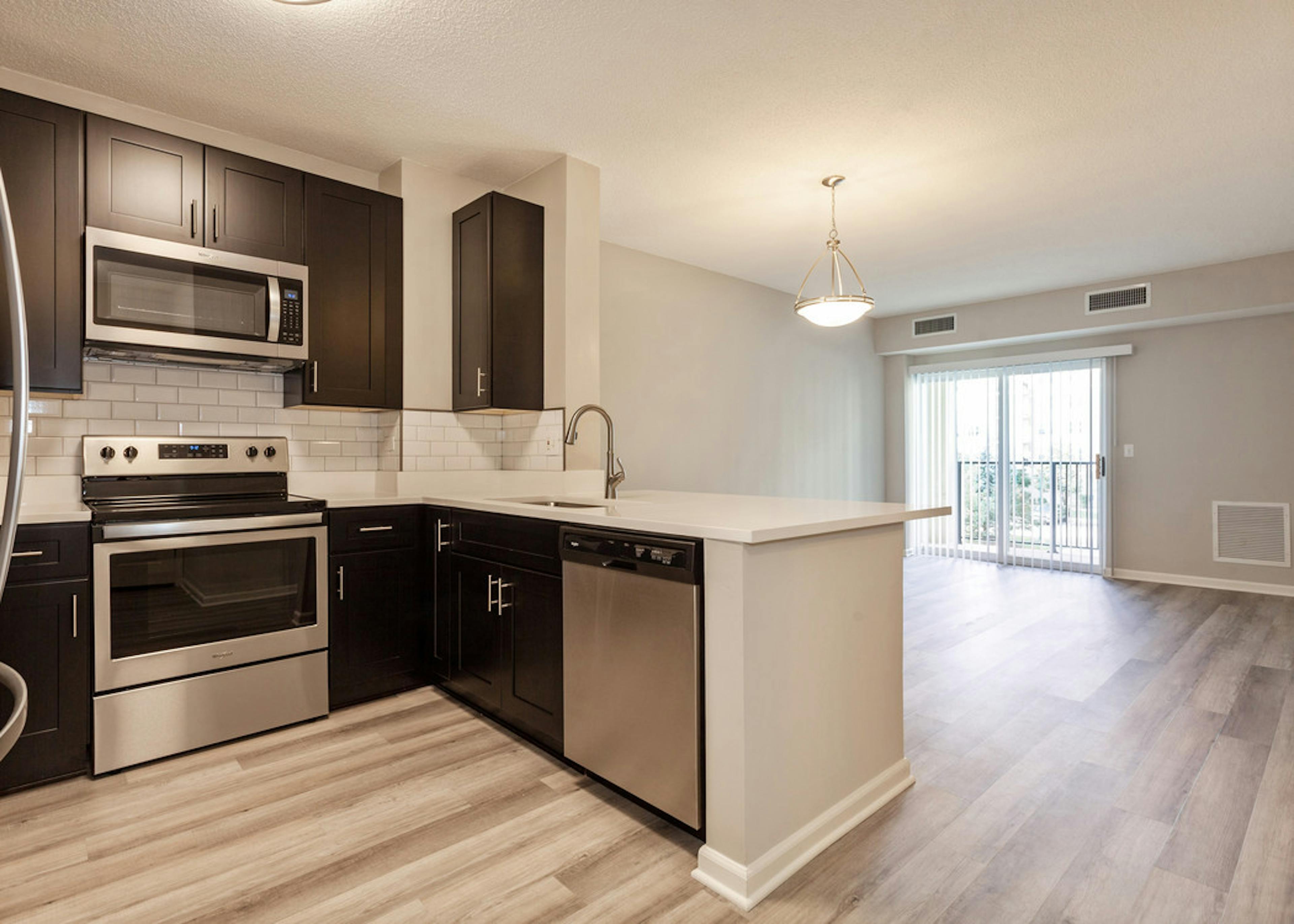 AMLI at Seven Bridges living room and kitchen with dark cabinetry and stainless steel appliances and wood-style plank floors