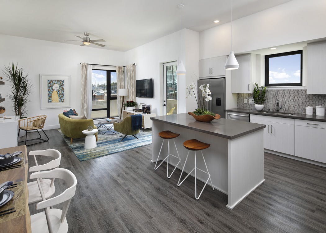 Interior of AMLI Marina Del Rey furnished apartment kitchen with white cabinetry, gray quartz countertops and living room