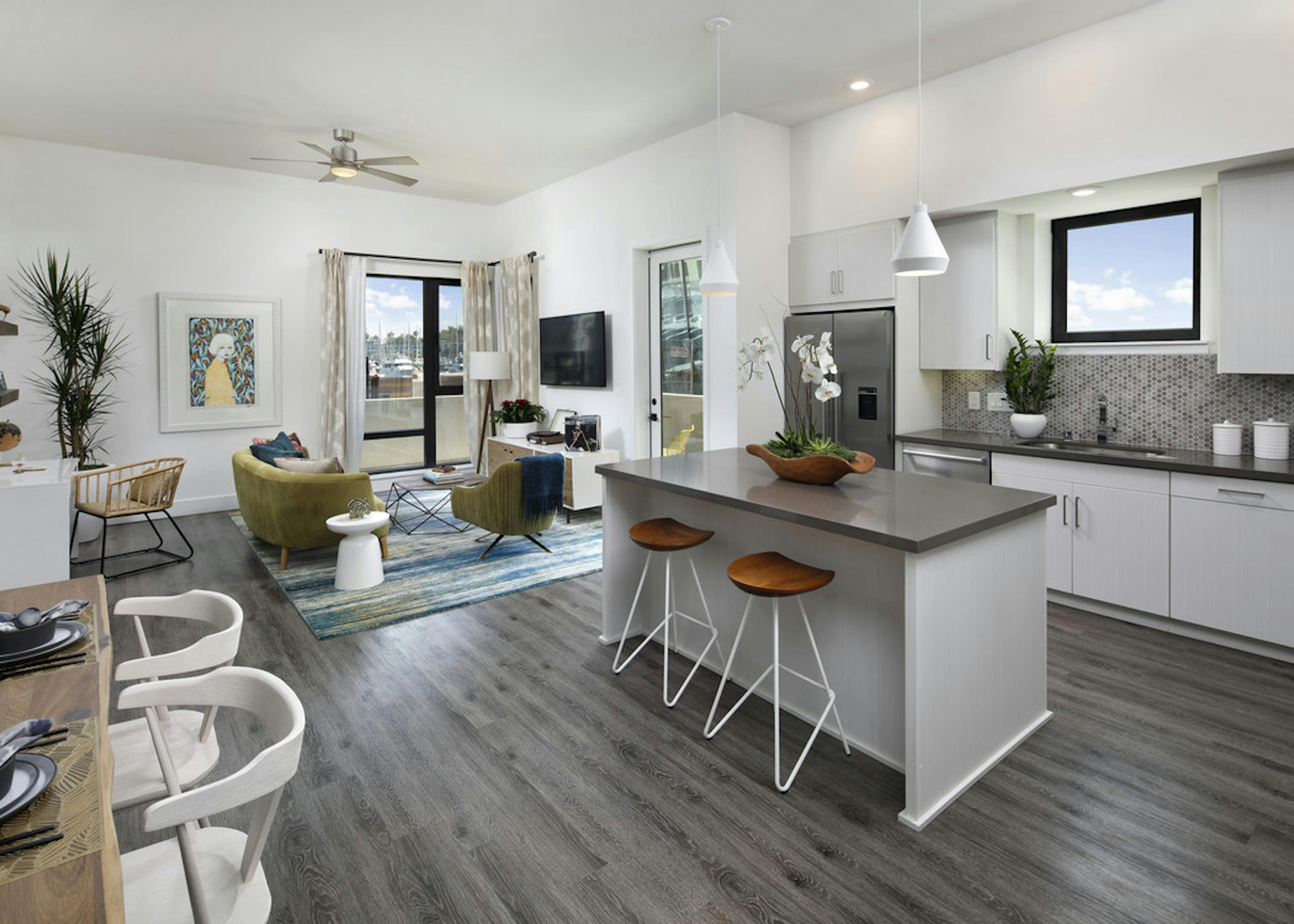Interior of AMLI Marina Del Rey furnished apartment kitchen with white cabinetry, gray quartz countertops and living room
