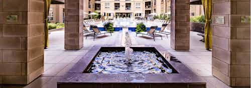 Exterior daytime view of AMLI RidgeGate centered fountain with connecting water channel to pool with blue tile trim surround