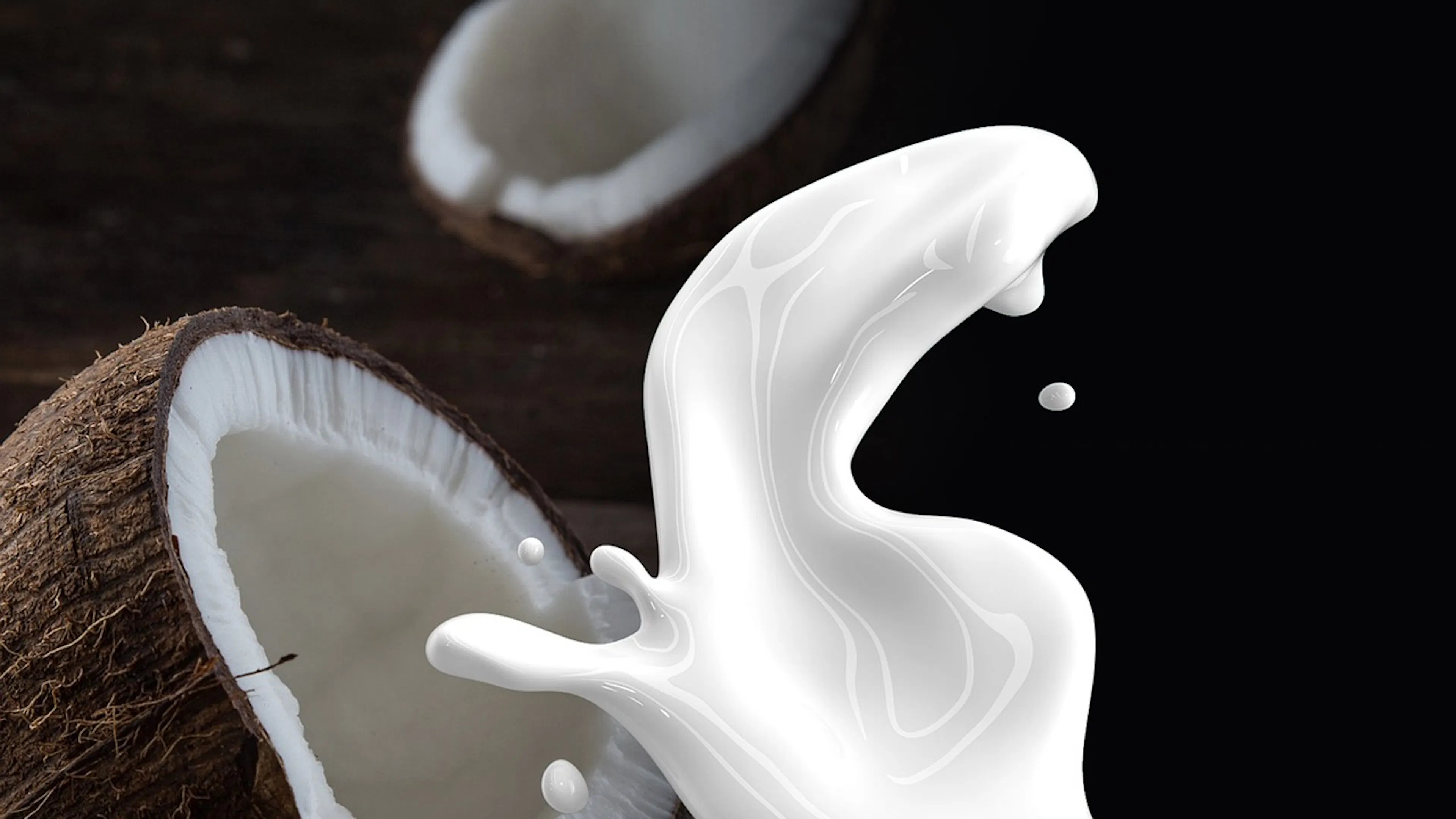 A coconut cracked open against a dark background with coconut milk splashing in an arc in the foreground