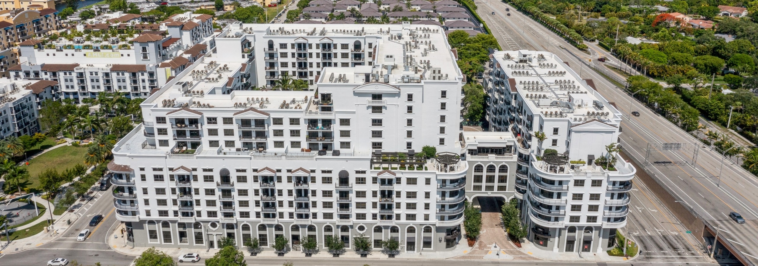 Aerial view of AMLI Joya apartment buildings surrounded by other buildings and roads and trees and blue sky in the distance