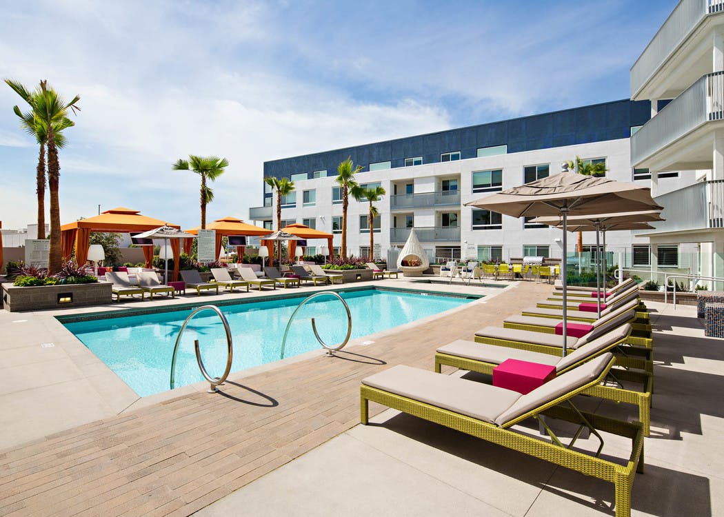 Daytime view of AMLI Lex on Orange swimming pool area with lounge seating, three orange cabanas and palm trees and blue sky