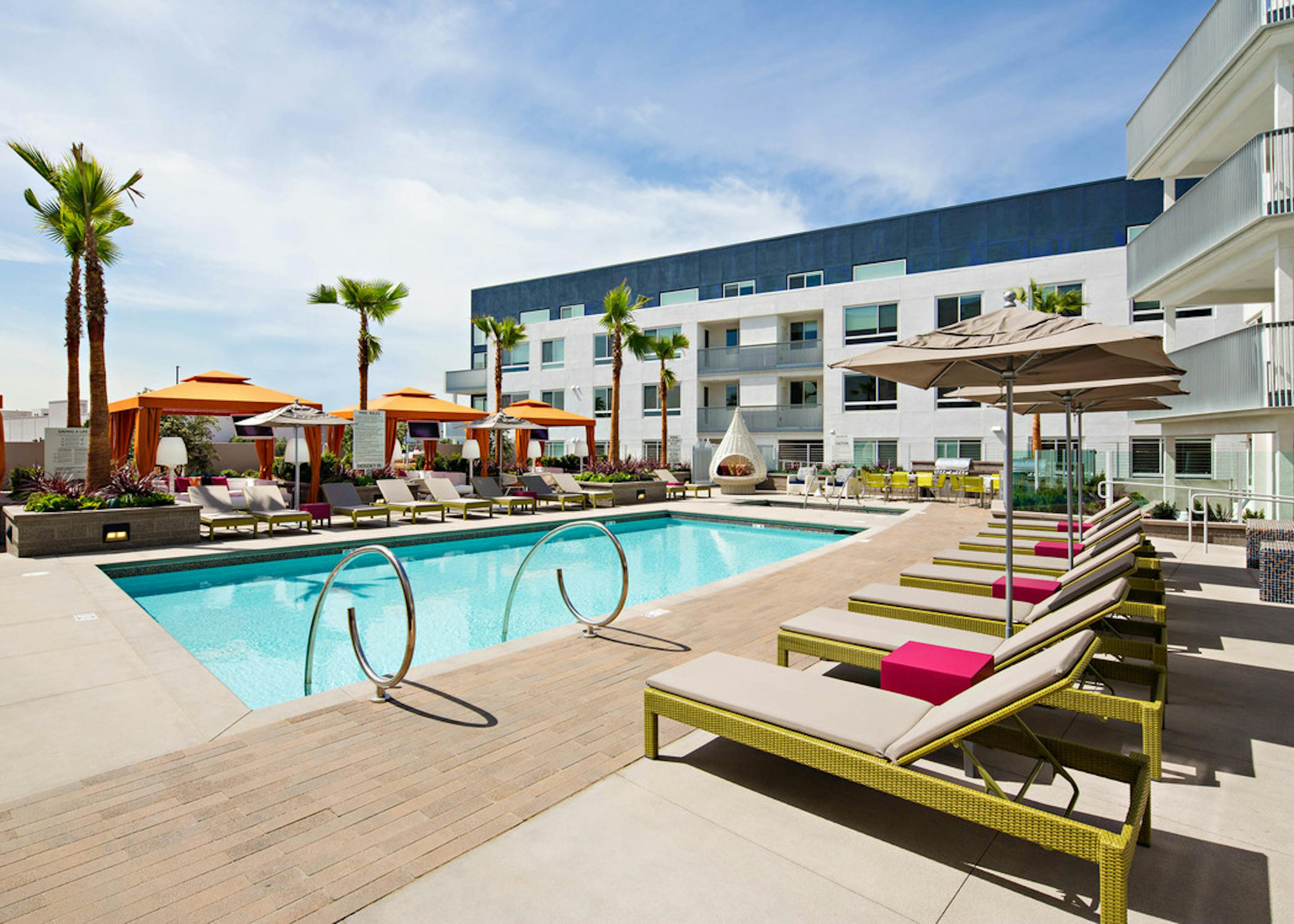 Daytime view of AMLI Lex on Orange swimming pool area with lounge seating, three orange cabanas and palm trees and blue sky