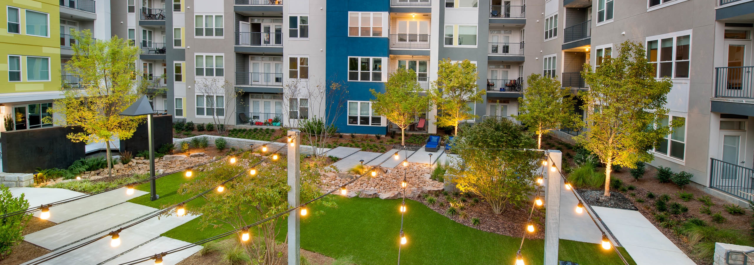 AMLI Piedmont Heights courtyard in the middle of the buildings containing grass and hanging lights and lined with small trees