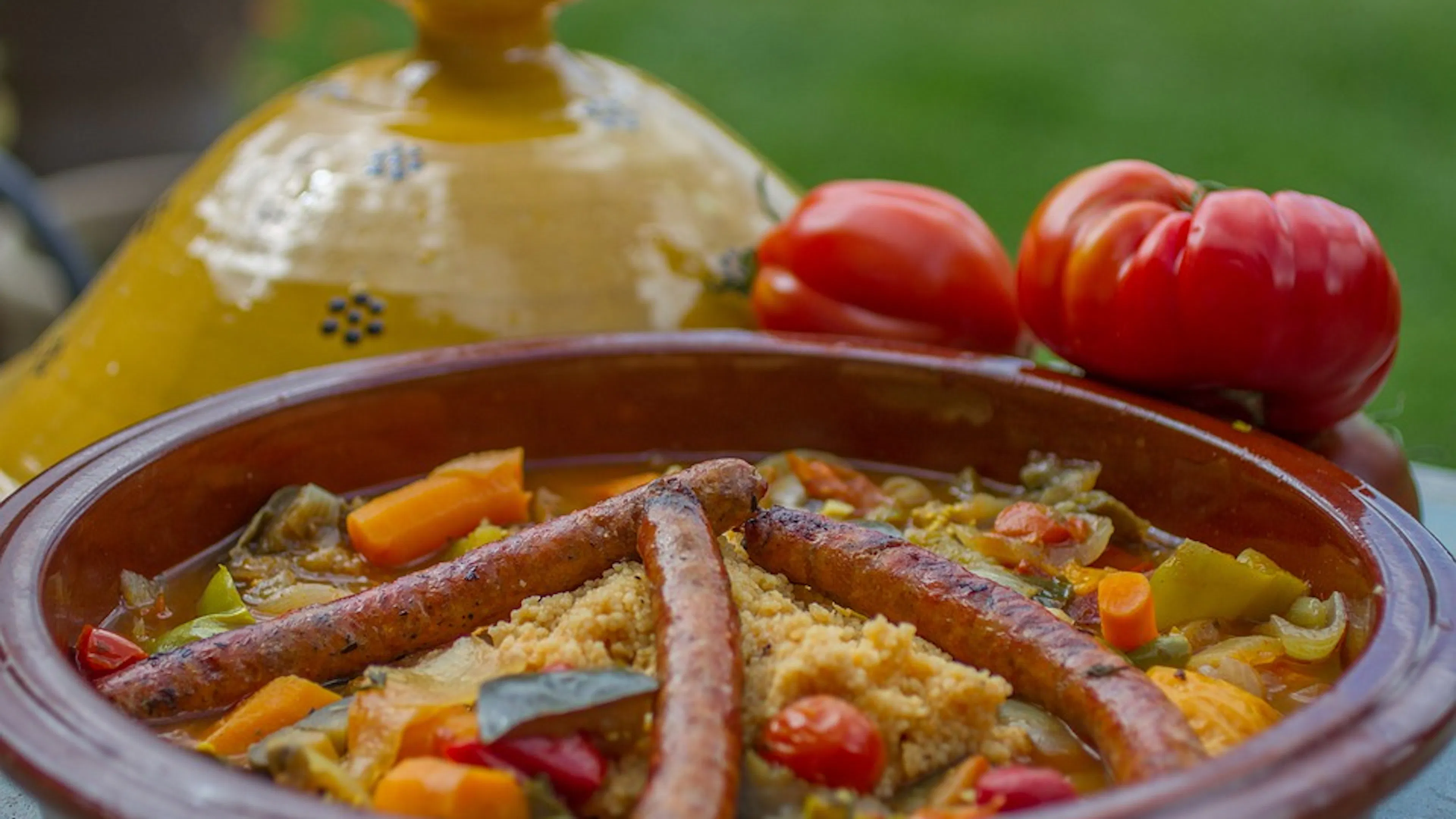 A clay tagine with a yellow glazed dome cover revealing couscous and vegetables inside
