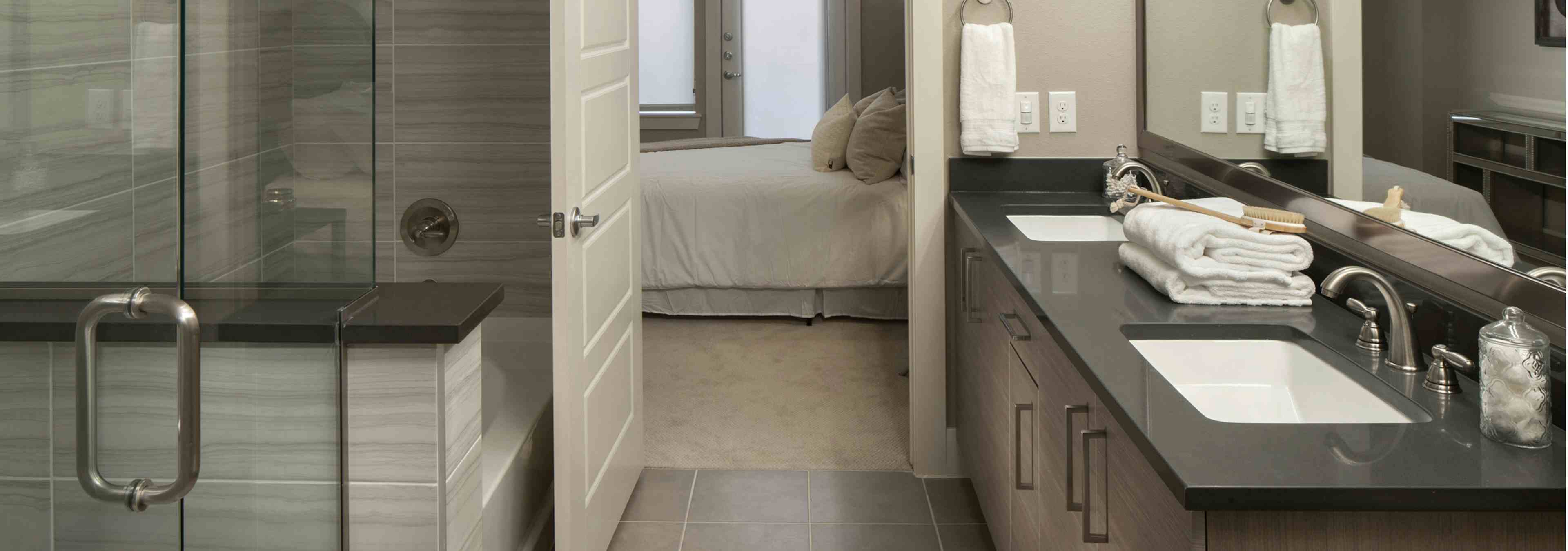 An interior view of the bathroom at AMLI Riverfront Green apartments with close up of glass shower door and view of bedroom