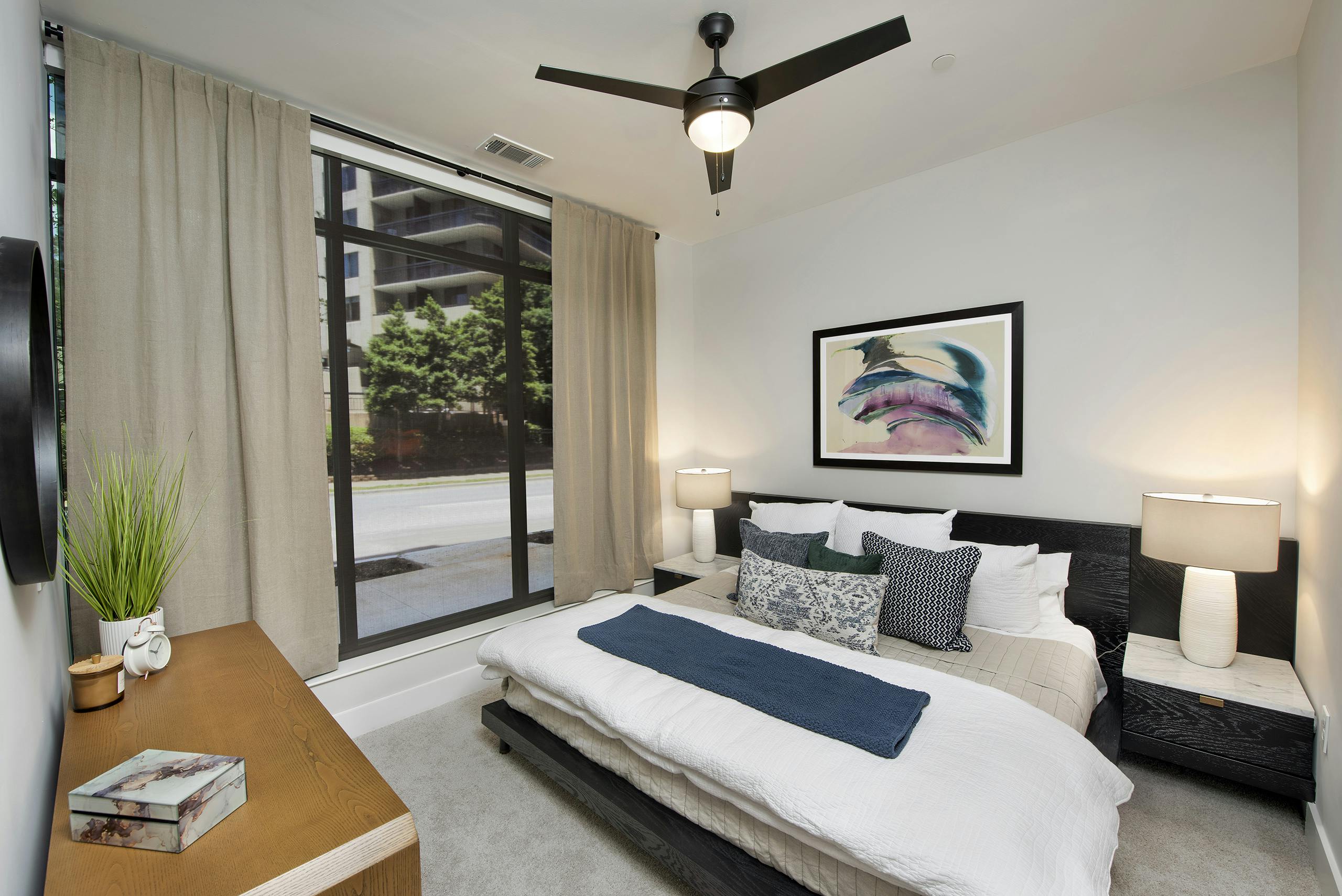 AMLI Flatiron bedroom with wood dresser and large dark wood bed with white and blue pillows and floor to ceiling window wall