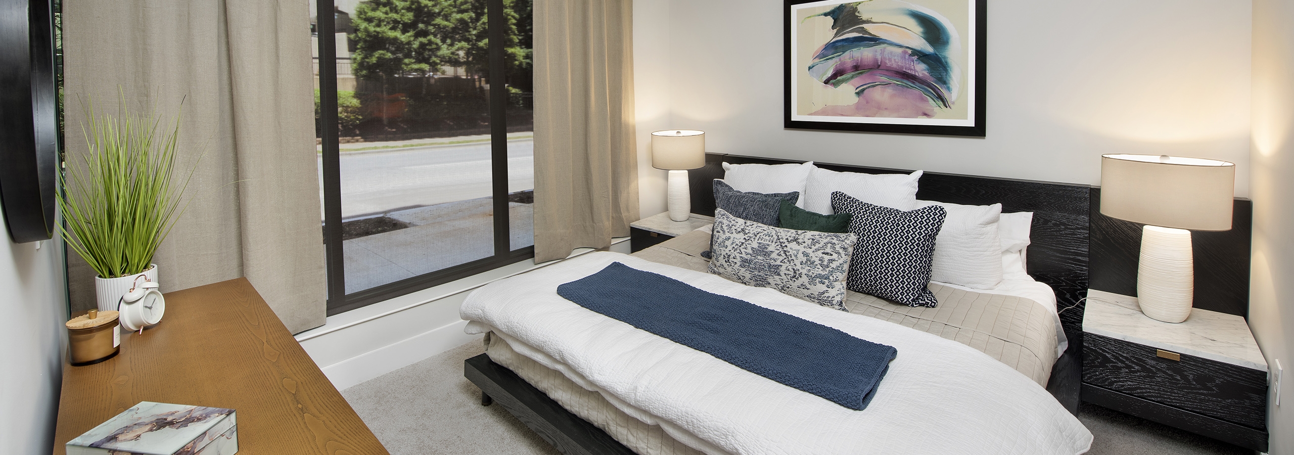 AMLI Flatiron bedroom with wood dresser and large dark wood bed with white and blue pillows and floor to ceiling window wall
