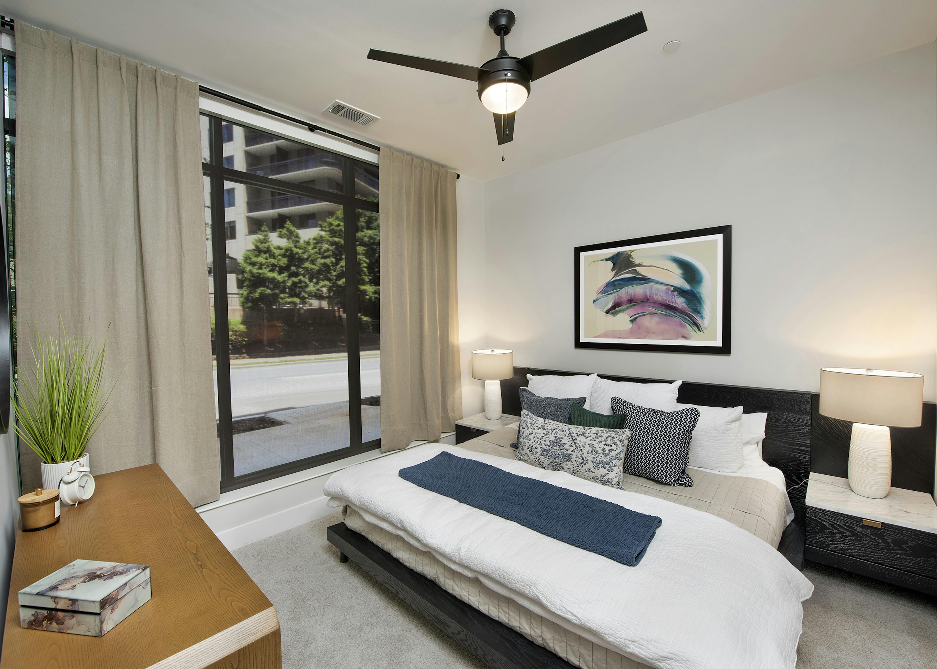 AMLI Flatiron bedroom with wood dresser and large dark wood bed with white and blue pillows and floor to ceiling window wall